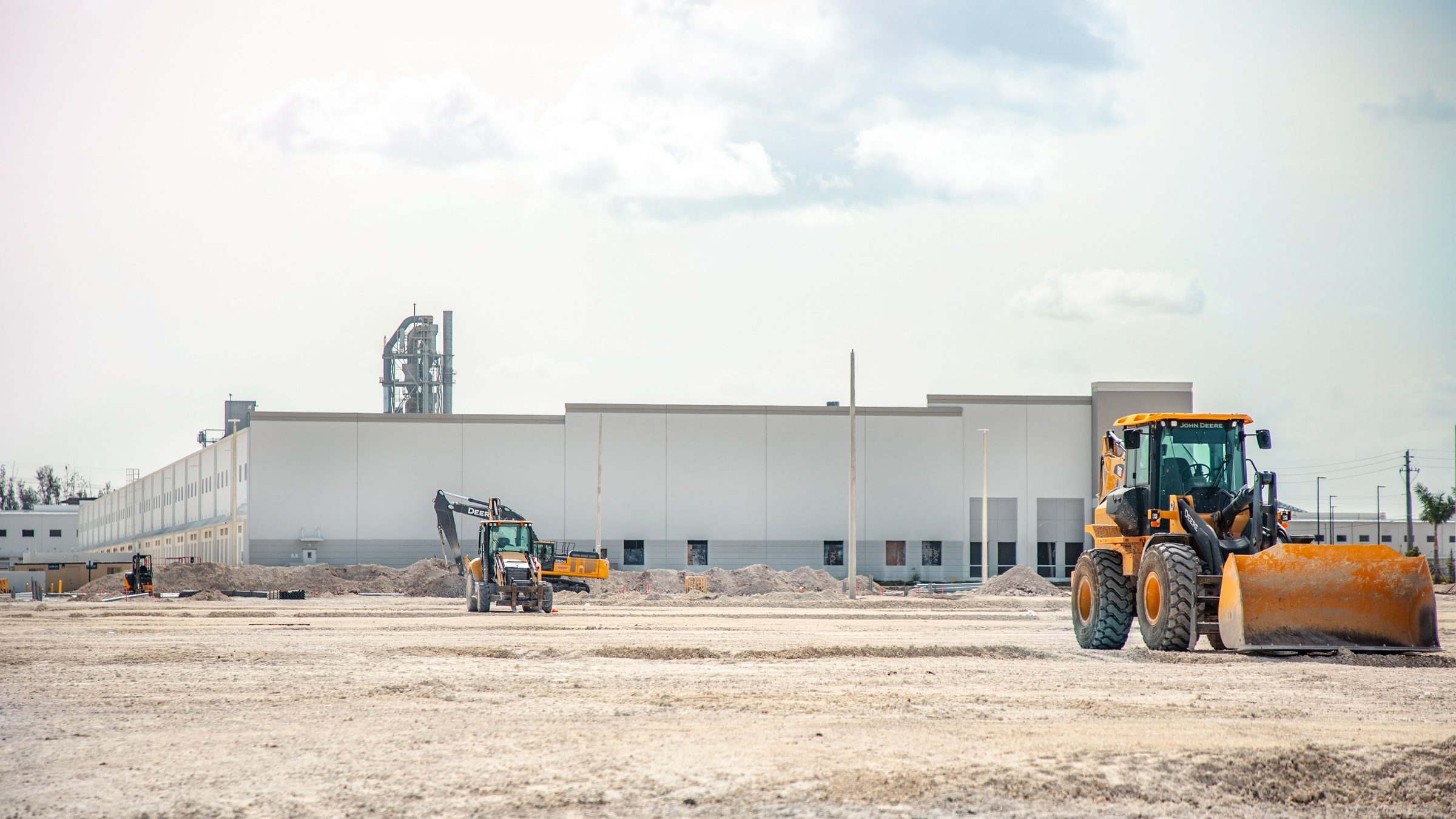 A commercial building under construction on a graded site, a wheel loader working in the foreground.