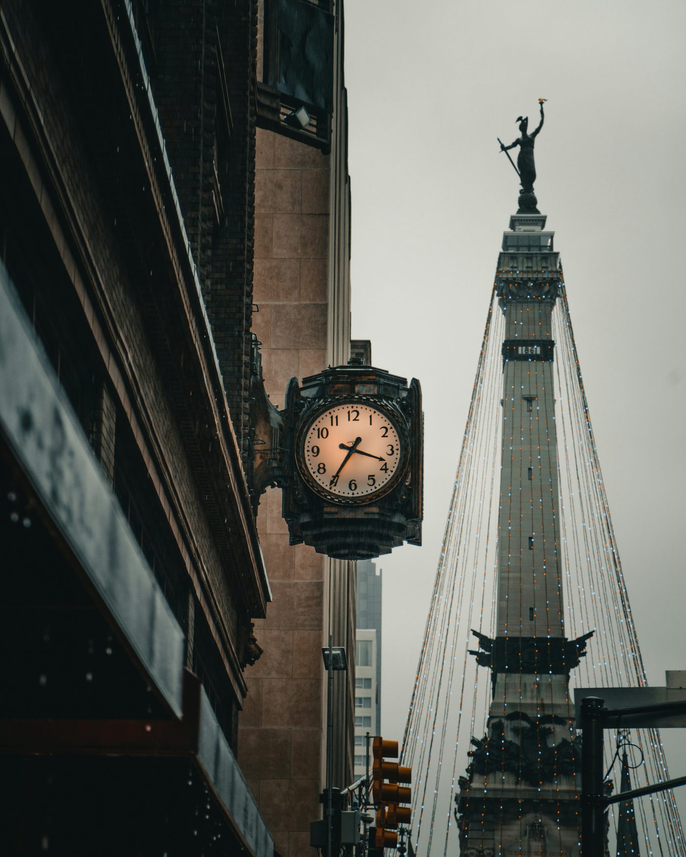The Soldiers and Sailors Monument on Monument Circle, lit for the holidays, seen past a street clock on a rainy evening.